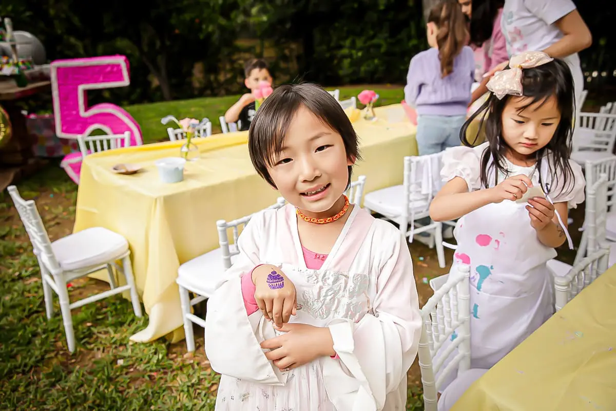 londons-5th-birthday-party-lacanada-kids-birthday-party-photographer-035 Smiling child shows cupcake hand stamp at an outdoor 5th birthday craft table