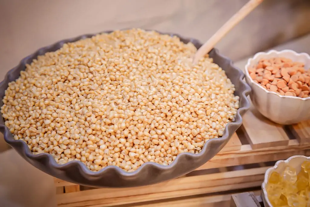 Heaping scalloped bowl of pale grains with a scoop, candies on the side.