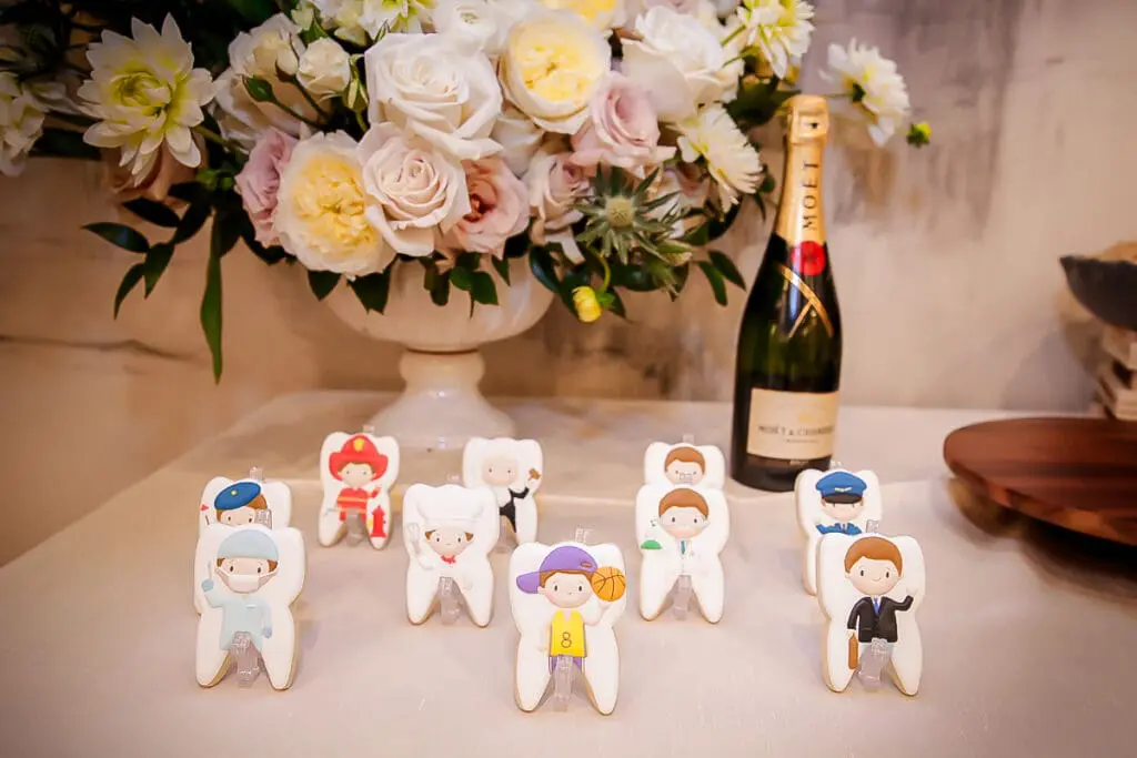 Cute tooth-shaped cookies with professions, flowers and champagne backdrop.