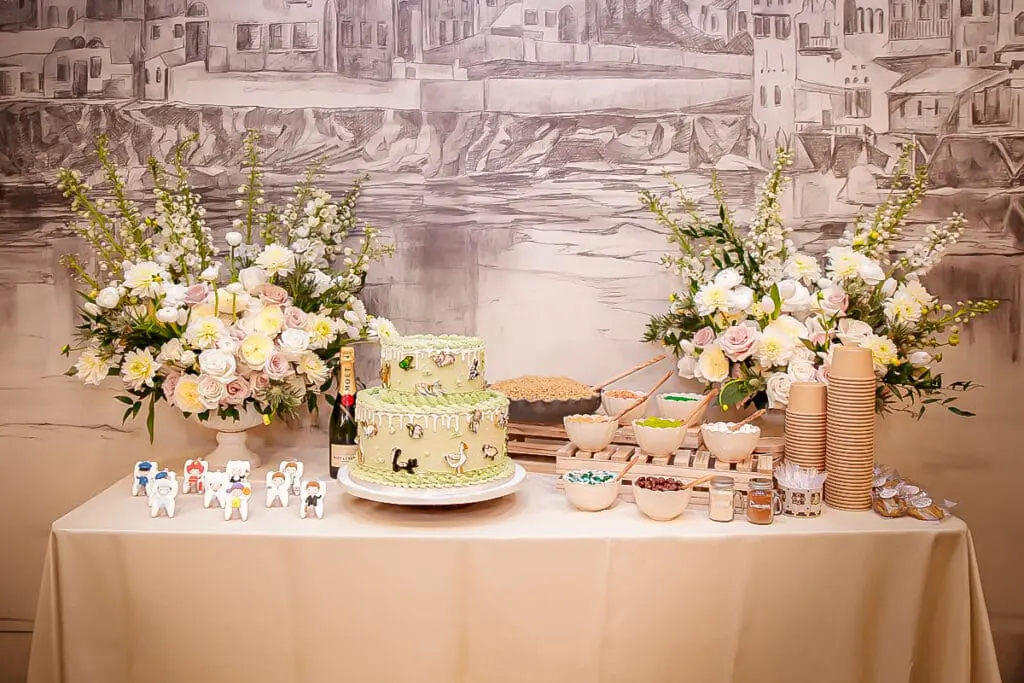 Festive dessert table with green tiered cake, lush flowers, and treats.