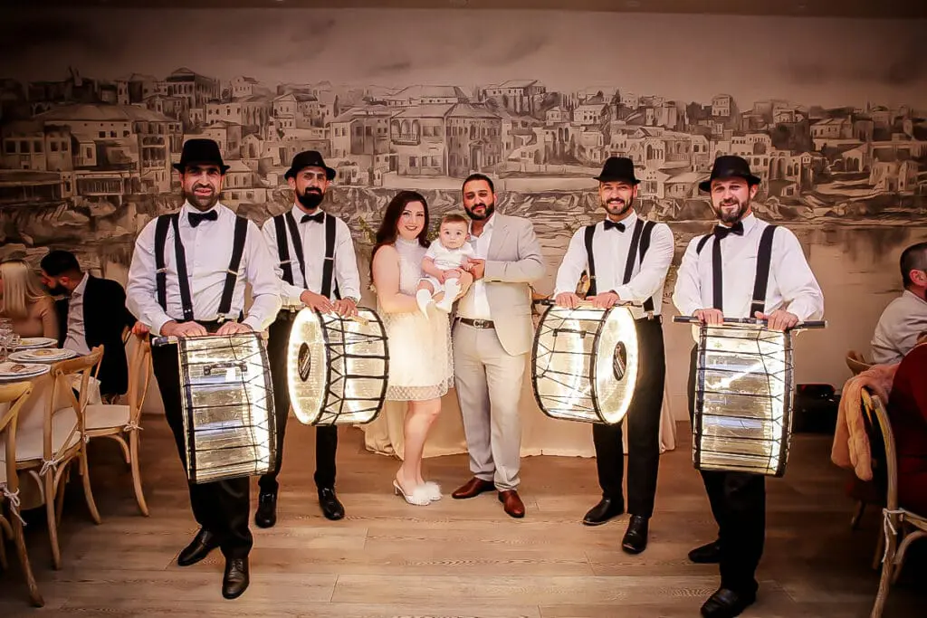 Smiling couple with baby and drummers holding glowing drums at a party