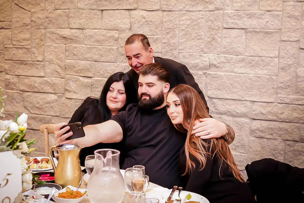 Group selfie at a dinner table, smiling by a stone wall.