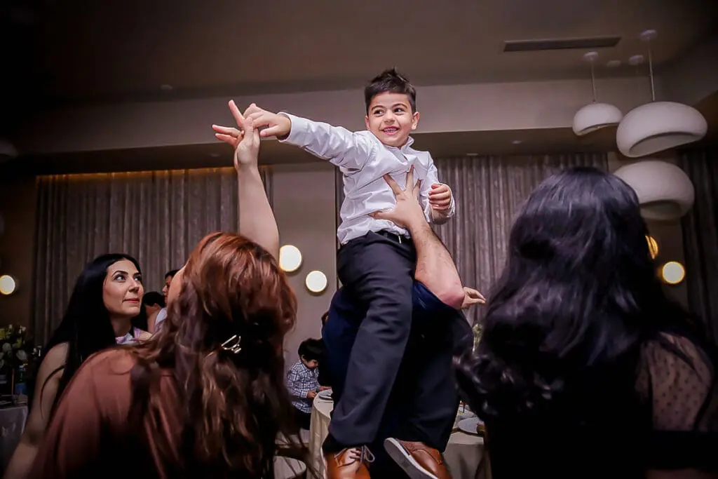 Smiling boy lifted high while guests cheer and dance