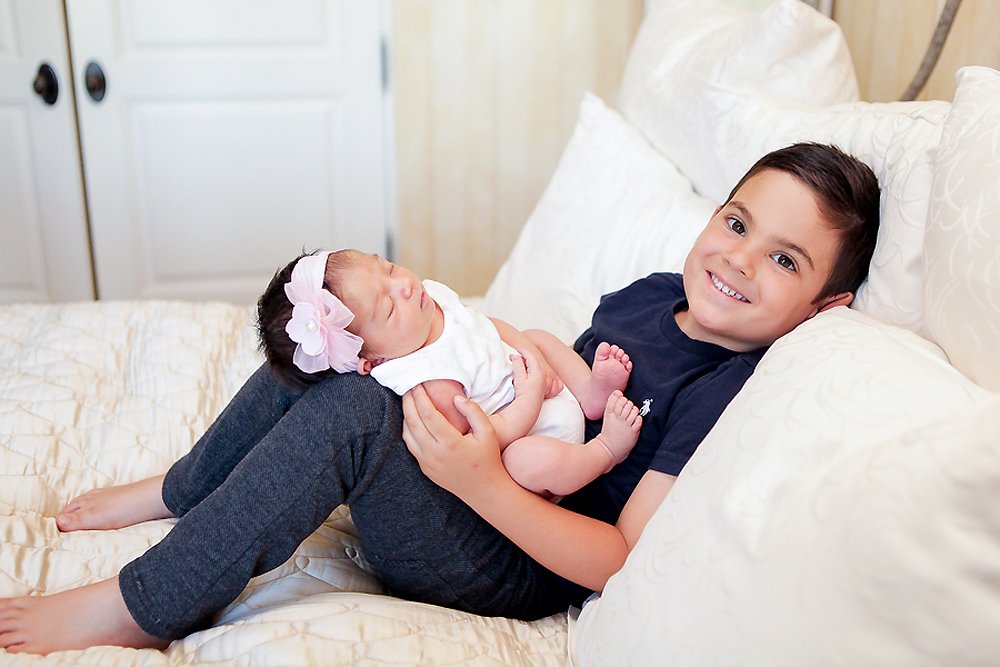 Brother holding his baby sister while laying in bed during her newborn photoshoot