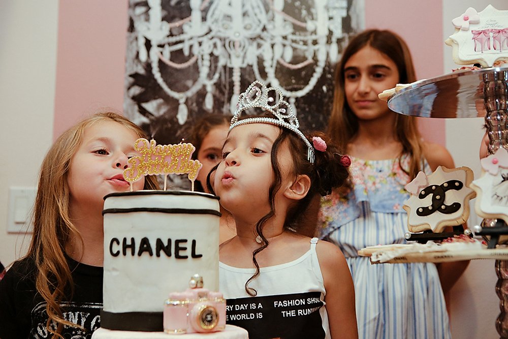 Birthday Girl is blowing out candles on her posy Chanel birthday cake.