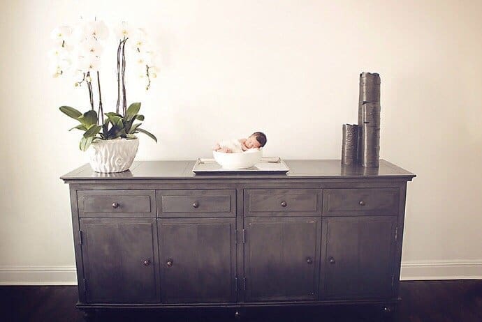Sleeping Newborn Baby resting in a bowl on a dining room buffet cabinet