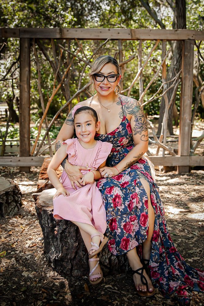 Family-Holiday-Portrait-Session-Descanso-Gardens Smiling adult and child in floral and pink dresses on a garden stump.