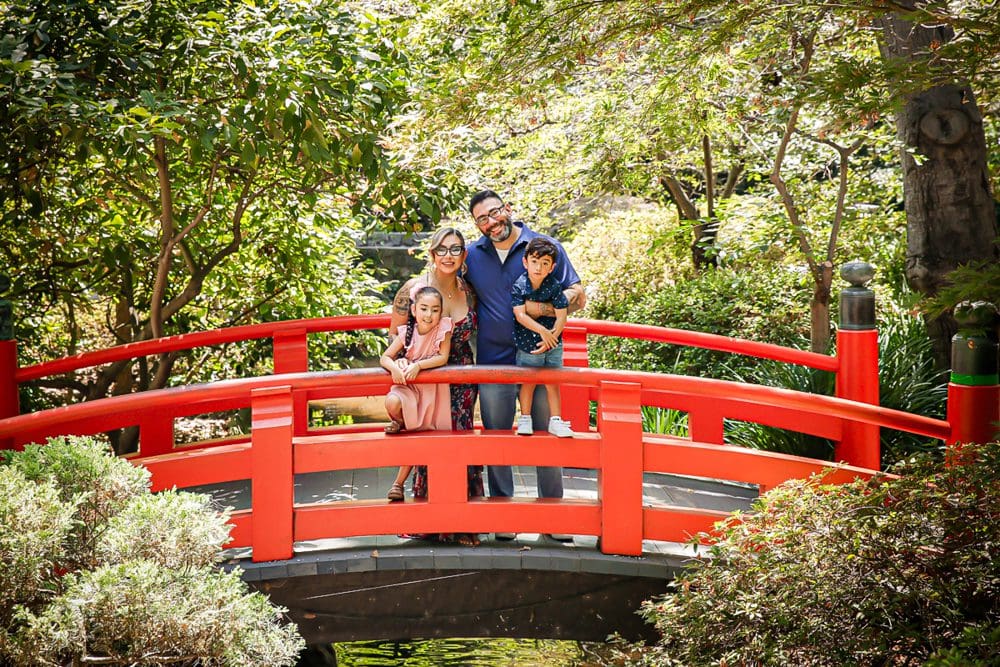 Smiling family on a bright red garden bridge surrounded by greenery