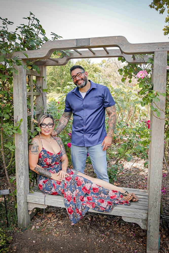 Family-Holiday-Portrait-Session-Descanso-Gardens Smiling couple relaxing on a wooden arbor bench in a sunny rose garden