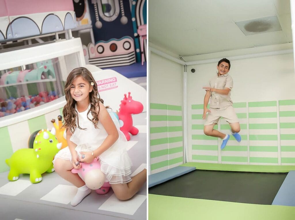 A smiling girl in a white dress sits on a pink inflatable toy beside a green one in a play area, captured by a kids birthday party photographer. Nearby, a boy in beige jumps on a trampoline against green and white striped walls.