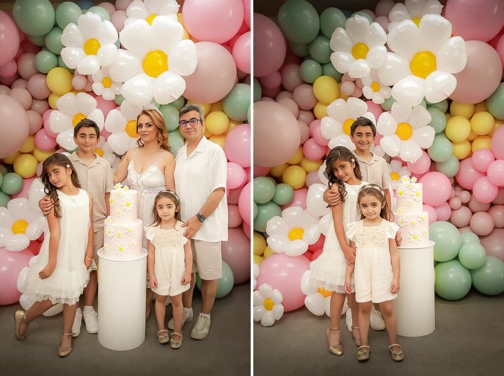 A woman and three children pose in front of a pastel balloon backdrop with large daisy balloons and a white cake decorated with small daisies. They are dressed in light-colored, semi-formal clothing.