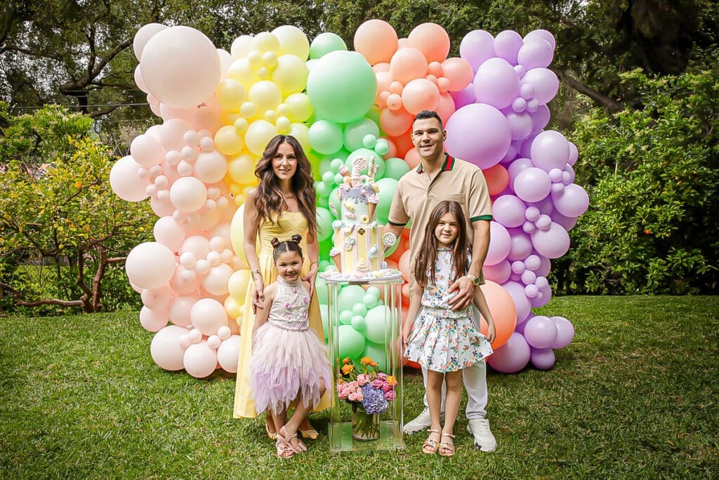 Family posing by a pastel balloon arch and tall cake at a 5th birthday.