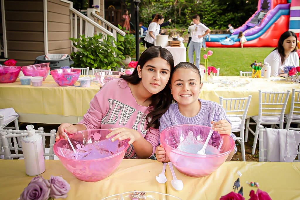 Two kids mix slime in pink bowls at a backyard birthday party