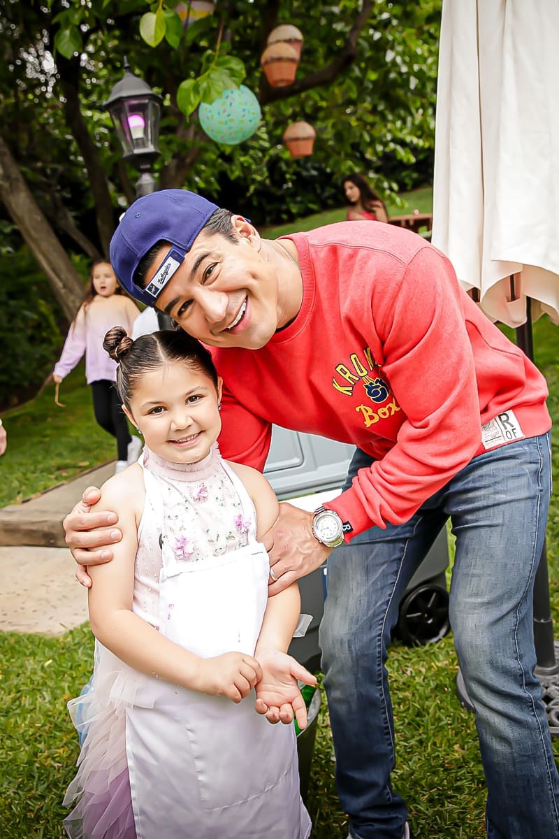 Smiling man hugs child in apron at a backyard birthday party.