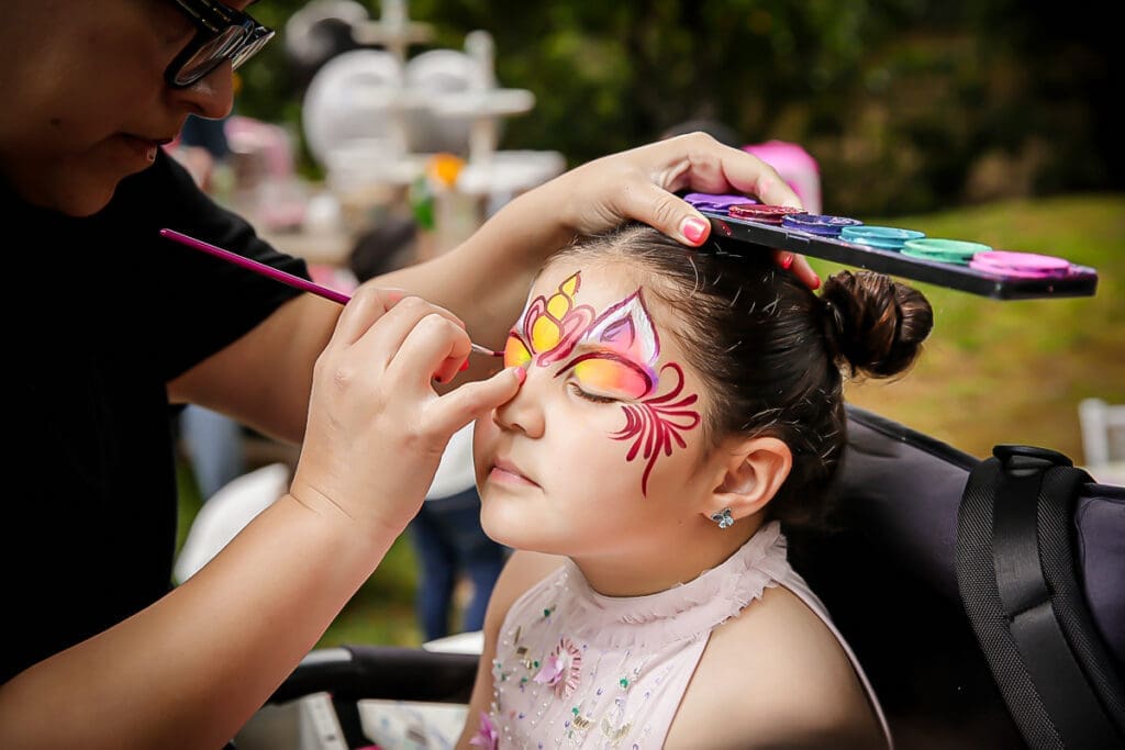 Child getting colorful face paint at a birthday party, eyes closed