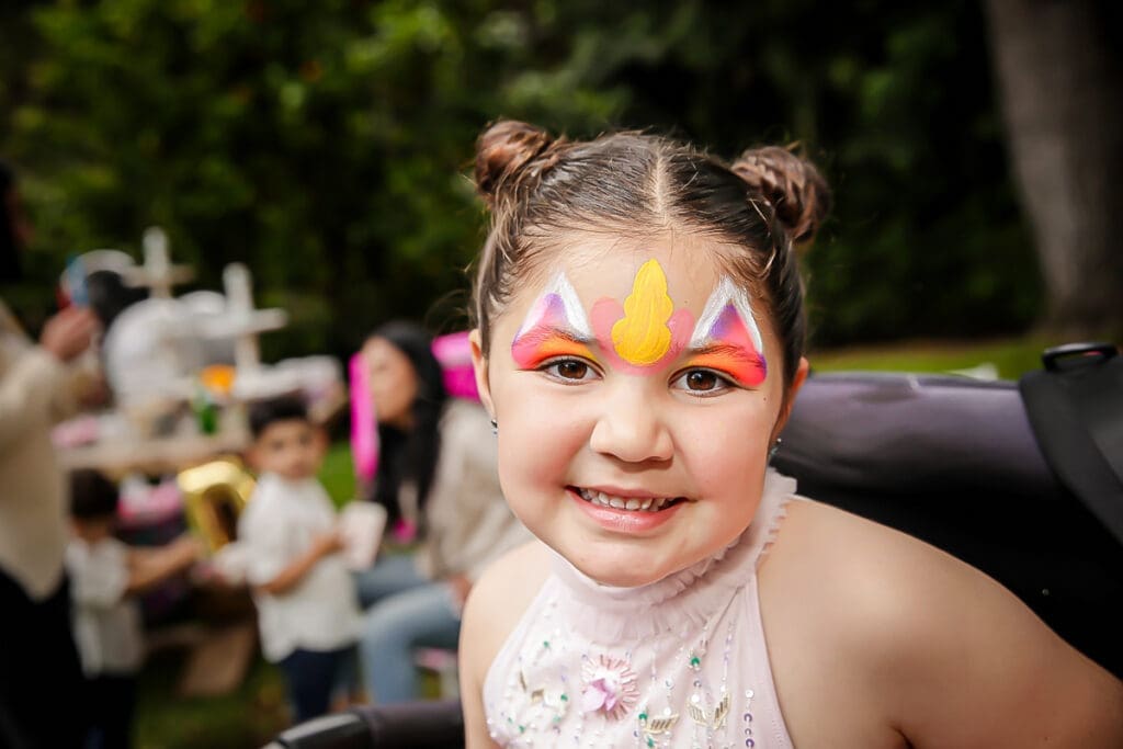 Smiling girl with unicorn face paint at a kids' birthday party.
