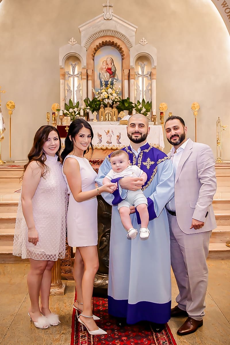 Smiling family with priest holding baby at ornate church altar.