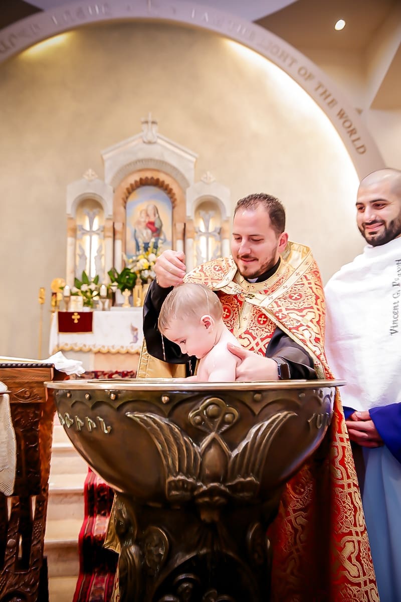 A priest gently baptizes a baby in a church font.