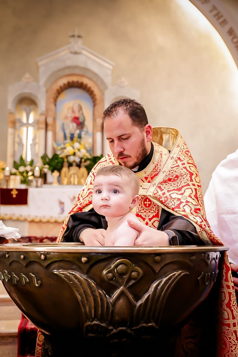 Sweet baby in an ornate basin, guided by a robed officiant in a bright church