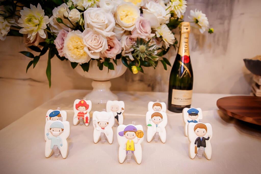 Cute tooth-shaped cookies with professions, flowers and champagne backdrop.